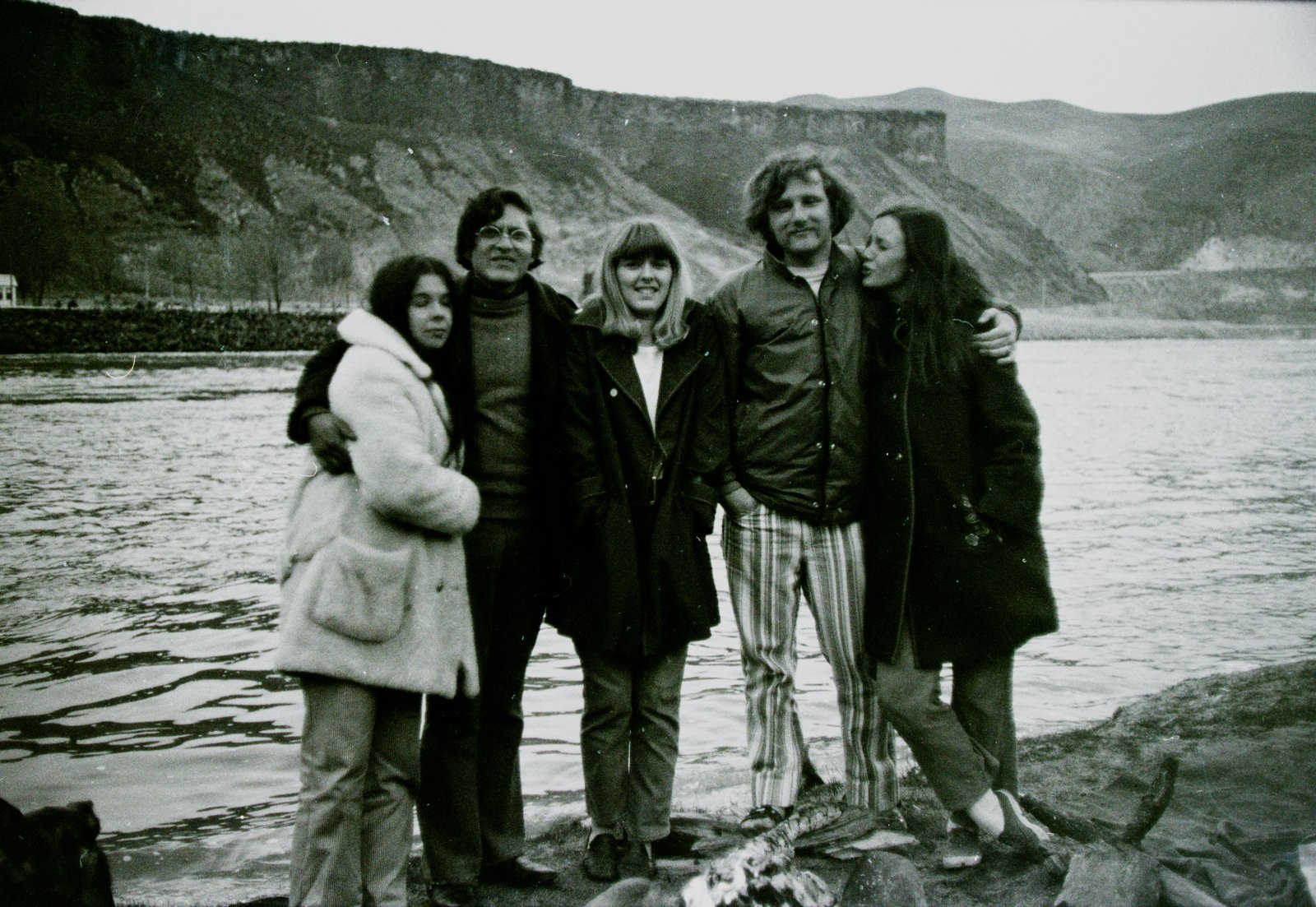 Five young friends arm in arm on a riverbank with cliffs behind